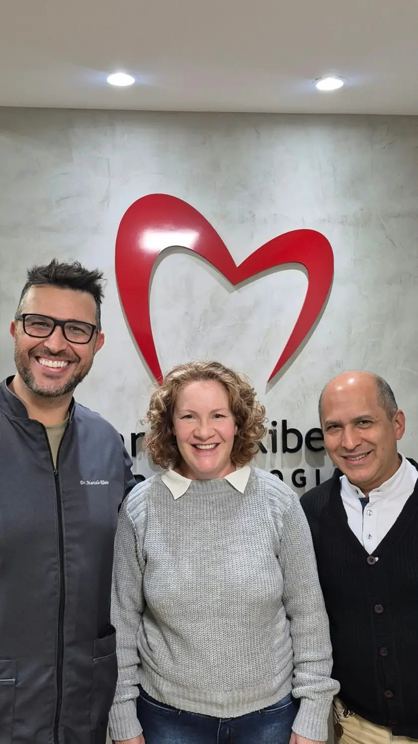 Paciente sorrindo entre o Dr. Marcelo Ribeiro e um acompanhante no consultório
