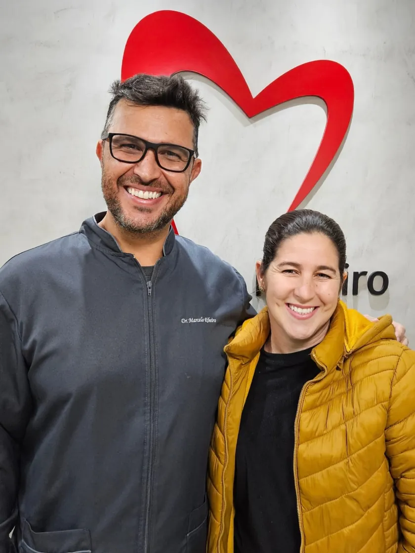 Paciente de jaqueta amarela sorrindo ao lado do Dr. Marcelo Ribeiro